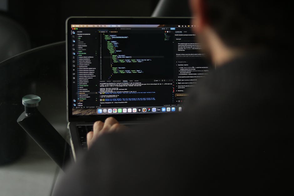 A computer monitor displays lines of programming code with syntax highlighted in various colours such as green, blue, pink, and white, on a black background. To the left of the screen, a light grey co